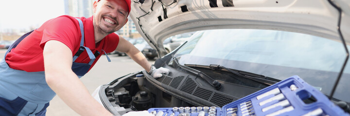 Smiling repairman in uniform fixing car with tools