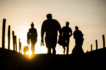 silhouette of a group people walking through the dunes to the beach during sunrise