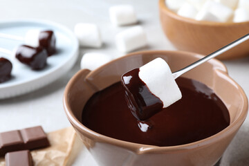 Dipping marshmallow into melted dark chocolate, closeup