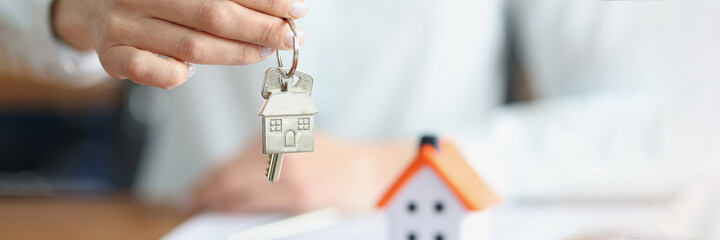 Female hand holding keys with keychain near toy house closeup