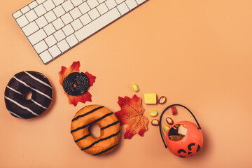 Fall Halloween Background Small Jack-O-Lantern Pumpkin Basket with Candy Autumn Leaves Laptop Computer Keyword Tasty Dinuts Orange Background Top View Copy Space