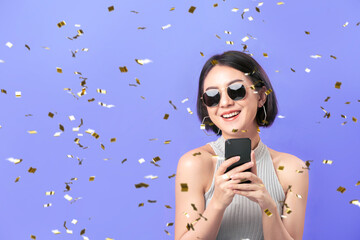 Young Asian woman using smartphone with confetti falling on purple background.