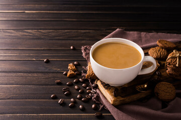 A cup of coffee mixed with milk or cream is placed on a dark wooden floor.