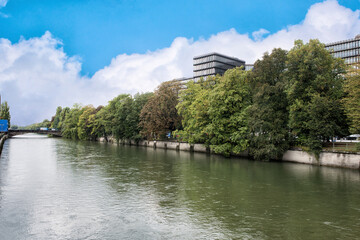 Fototapeta na wymiar A riverside of Isar river in munich with green trees under blue cloudy sky.