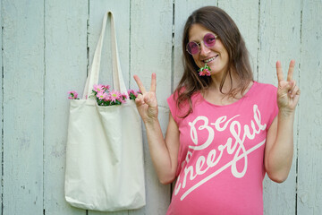Smiling hippie woman in pink t-shirt with Be Cheerful inscription and pink round glasses, made...
