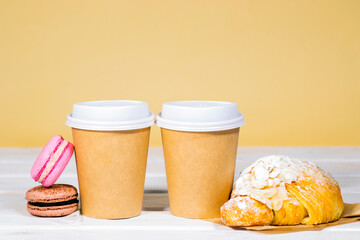 Take Away Coffee in paper eco cup with almond croissant and french macaroon on wooden and light orange background, Fast food, Copyspace, Coffee bean