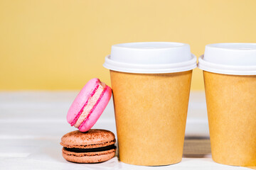 Fototapeta na wymiar Take Away Coffee in paper eco cup with two french macaroon on wooden and light orange background, Fast food, Copyspace, Caffeine Drink take away