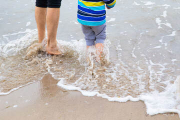 A father with a little boy walks into the cold waves in clothes, having fun