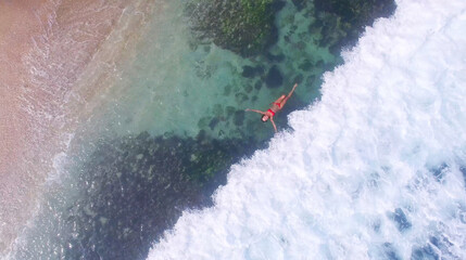 Young and beautiful fashion female model in red bikini lying on the waves in the sea. Fashion shooting. Aerial video in Indonesia Bali. Relaxing on vacation