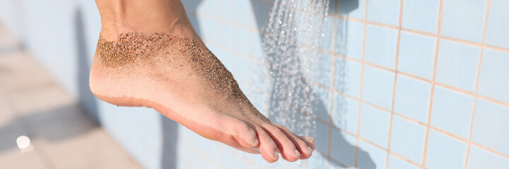 Woman washing her foot from sand under shower on beach closeup