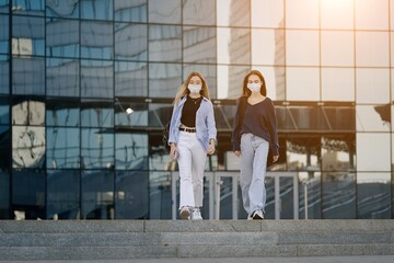 Two teenage students friends girls in wearing face mask going back to school after covid 19 lock down, carrying school bag    