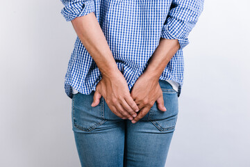 Man suffering from hemorrhoids and anal pain while posing on white background. Male putting his hands at the painful area. Stock photo - obrazy, fototapety, plakaty
