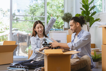 Happy couple asian young woman, man.packing stuff clothes, give second hand for donate, check list object in cardboard box. Moving, preparing in new home, apartment relocation. Mortgage, real estate.