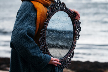 Woman holding vintage mirror near a sea.