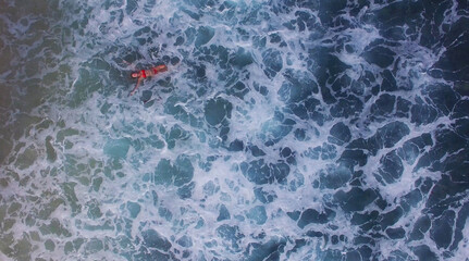 Young and beautiful fashion female model in red bikini lying on the waves in the sea. Fashion shooting. Aerial video in Indonesia Bali. Relaxing on vacation