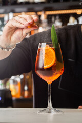 Bartender preparing on the counter Aperol Spritz, a classic refreshing Italian aperitif made mixing Aperol, Prosecco and sparkling soda.