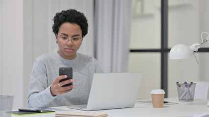 African Woman with Laptop using Smartphone at Work