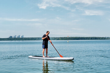 Asian older man on sup board on calm lake.