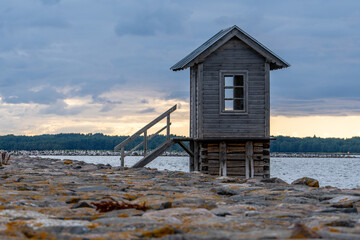 Fototapeta na wymiar Estonia, on the island of Hiiumaa, next to a rocky pier, there is a small wooden house rising above the water