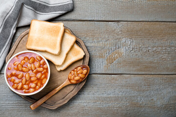 Toasts and delicious canned beans on wooden table, top view. Space for text