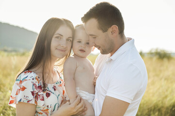 Portrait of young happy family holding in hands cute toddler son at summer day on field