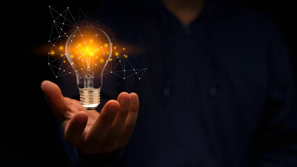 Close up hand of man holding illuminated light bulb in black background. idea, innovation,...