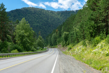 highway road and mountain peaks on the background of a blue sky with clouds
