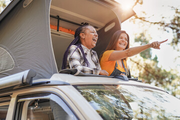 Senior multiracial friends enjoy vacation in the nautre with mini van - Mature women on a road trip with camper