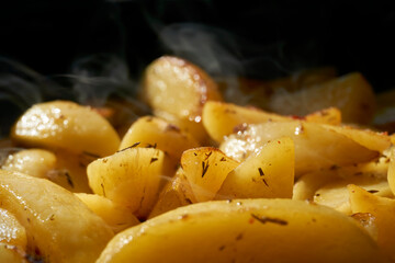 Hot steaming baked potato wedges with fresh herbs agent a dark background.      
