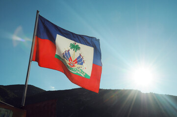 Haitian flag blowing in the breeze with the Haitian mountains behind and a sunset casting rays of light