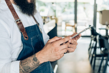 Unrecognizable Barista Using Digital Tablet in a Cafe.

Close up photo of male hands with tattoo holding digital tablet and reading online order or watching something while working in the restaurant.
