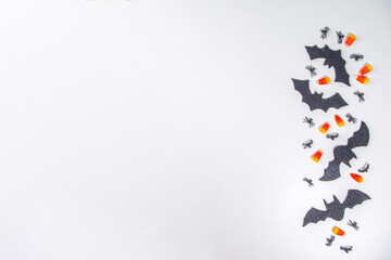 Fototapeta premium Halloween frame background. Bat and spider decorations with traditional trick o treat candy corn on white background. Halloween greeting card. Flat lay top view copy space