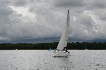 Sylwetka samotnie żeglujacego jachtu kabinowego. Mazury, krajobraz. Deszczowy dzień. © Lidia
