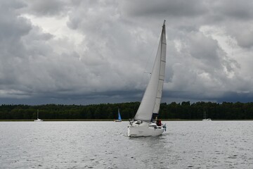 Sylwetka samotnie żeglujacego jachtu kabinowego. Mazury, krajobraz. Deszczowy dzień.