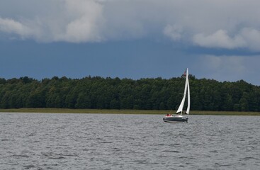 Sylwetka samotnie żeglujacego jachtu kabinowego po jeziorze. Mazury, krajobraz. © Lidia