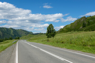 highway road and mountain peaks on the background of a blue sky with clouds