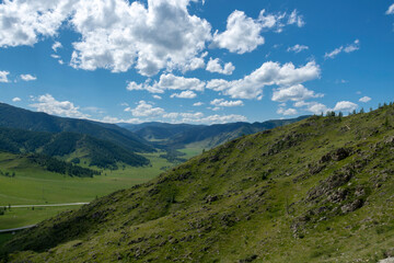mountain peaks against a blue sky with clouds and a green valley