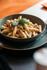 Penne pasta with cheese and herbs in black bowl