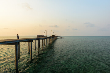 Fototapeta na wymiar Long wooden bridge go to the sea in beautiful tropical island at sunset.