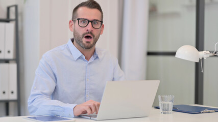Middle Aged Man with Laptop feeling Shocked 