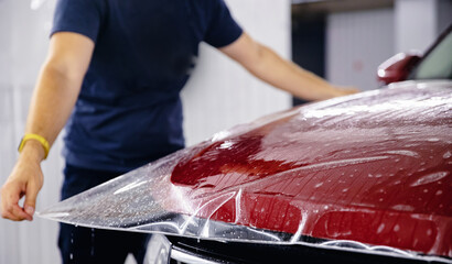 Process of pasting hood of red car with protective vinyl film from gravel chips and scratches....