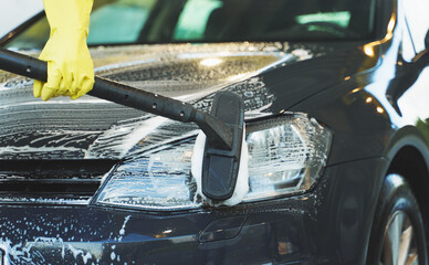 Woman in uniform cleaning car with brush. Car wash service.