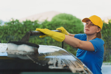Woman in uniform cleaning car with brush. Car wash service.