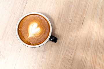Latte coffee or cappuccino coffee in black cup with beautiful heart latte art on wooden table.