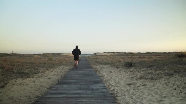 Hombre corriendo por un camino de tablas de madera direcci&oacute;n a la playa 