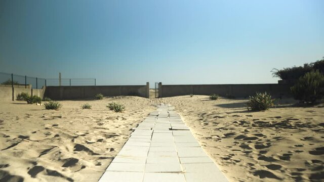 Camino de losas en la arena con una valla al fondo que da a la playa