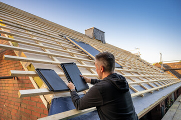 Roofer is putting flat tiles on a new roof.