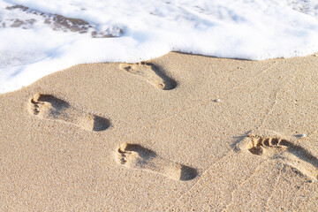 Human footprints on sandy beach with sea wave