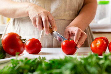 Chef slicing tomato using knife on the table in restaurant. Process of cutting and preparation food in kitchen.