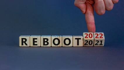 2022 reboot new year symbol. Businessman turns wooden cubes and changes words 'Reboot 2021' to 'Reboot 2022'. Beautiful grey background, copy space. Business, 2022 reboot new year concept.